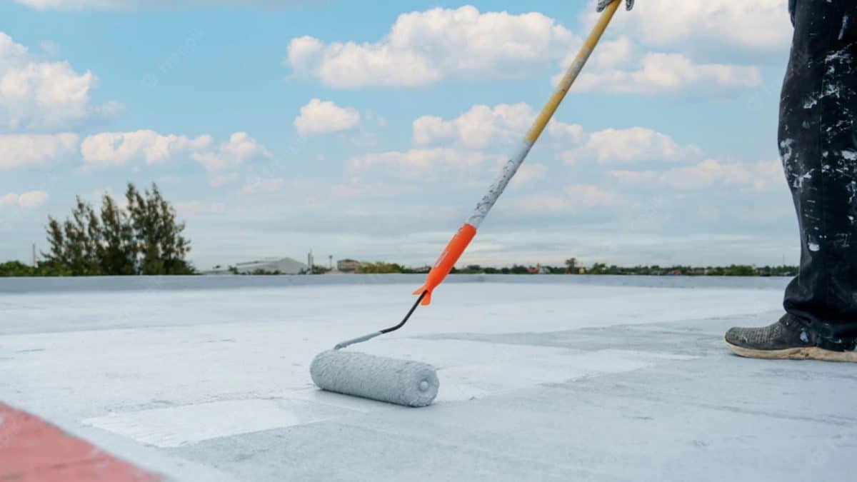 Worker applying white roof coating on a flat roof